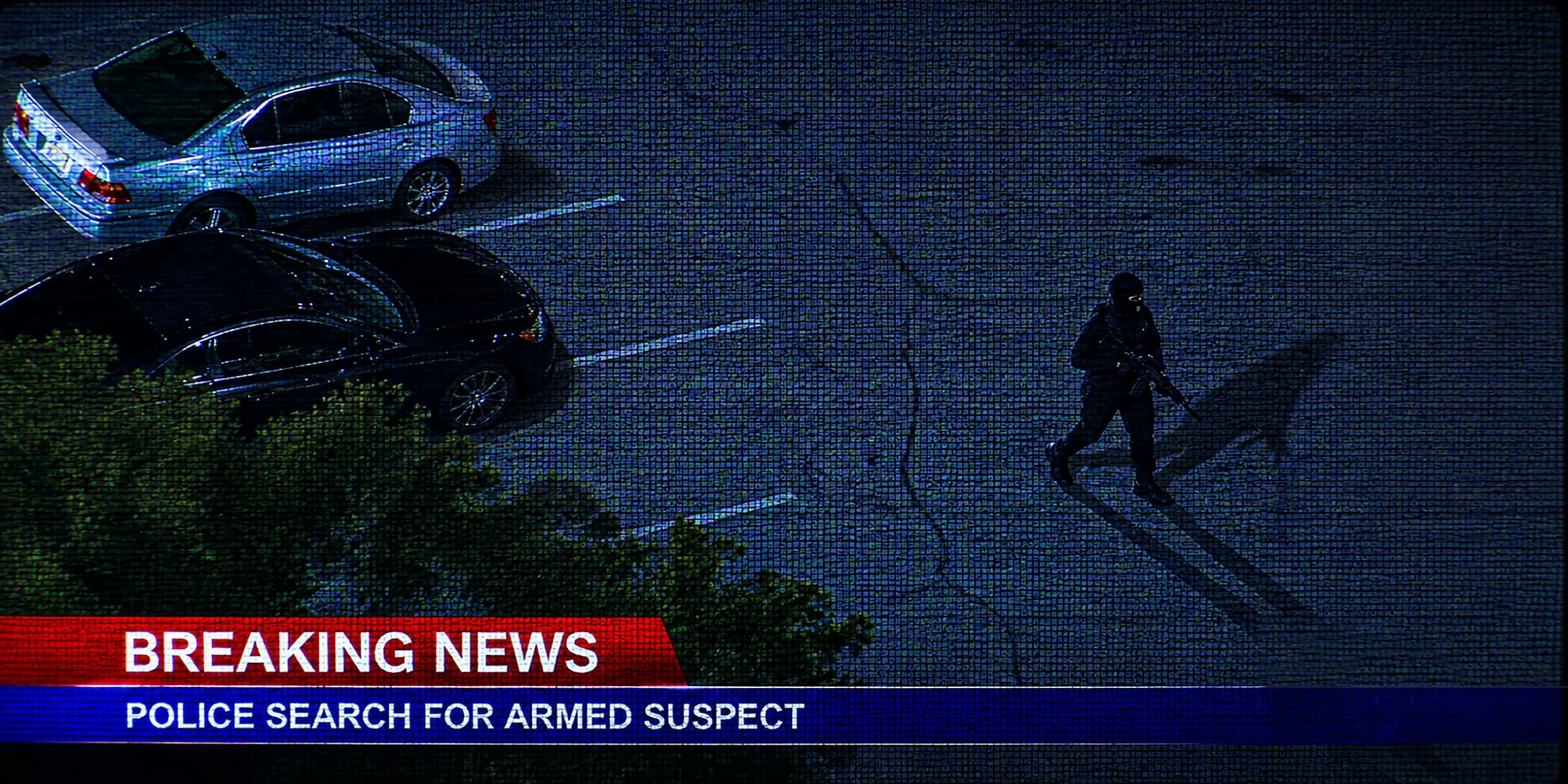 Aerial night view of a police search for an armed suspect, framed as a breaking-news broadcast